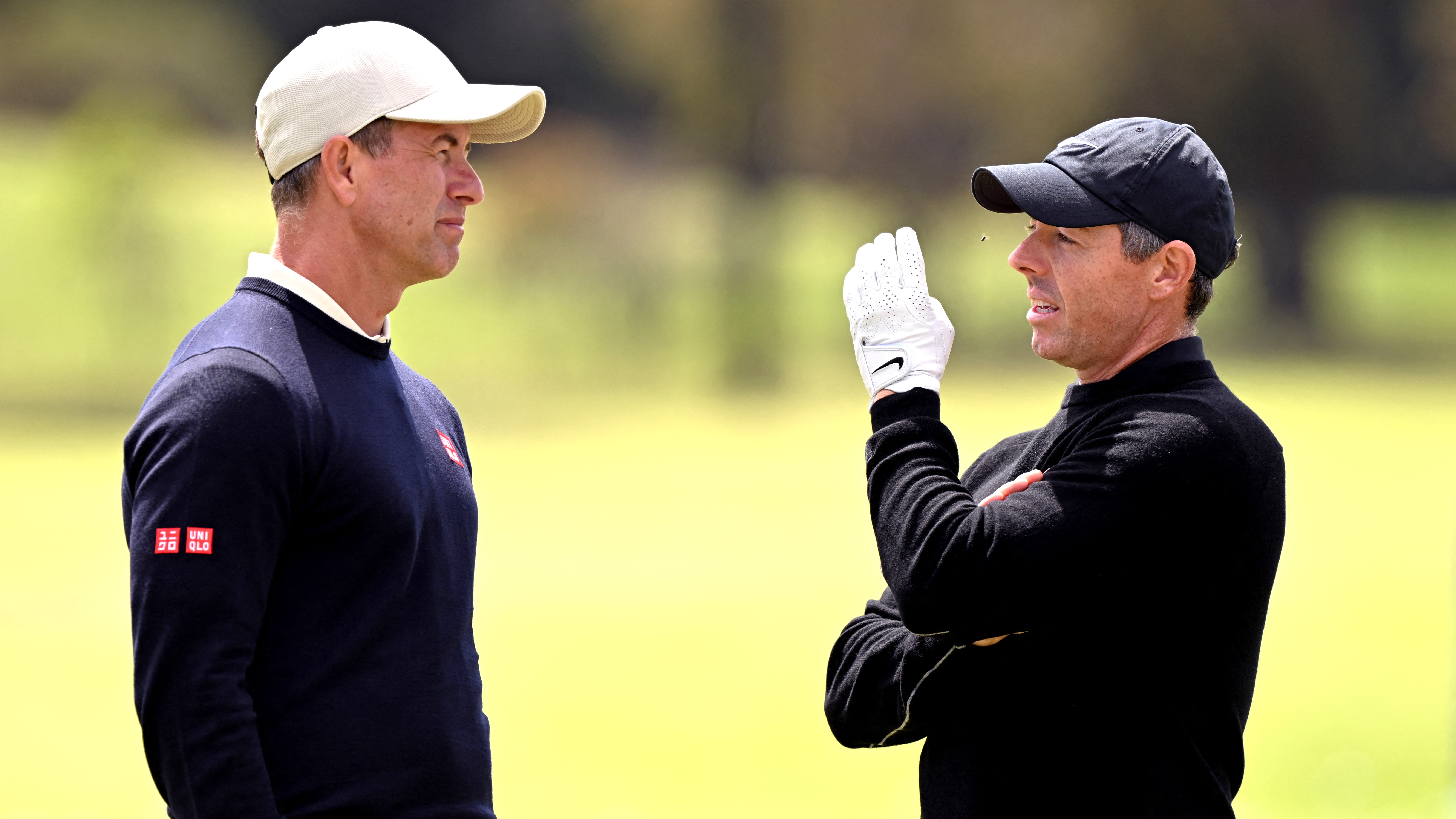 Rory McIlroy swats away a fly as he talks to Adam Scott during practice for the Australia Open