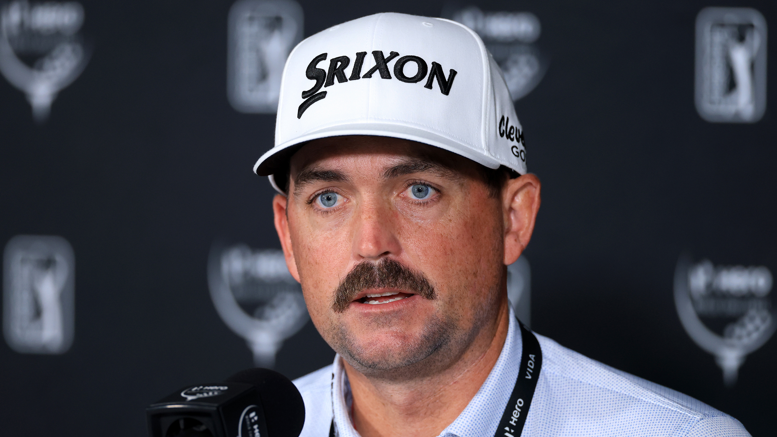 Keegan Bradley speaking at a press conference while wearing a white Srixon cap